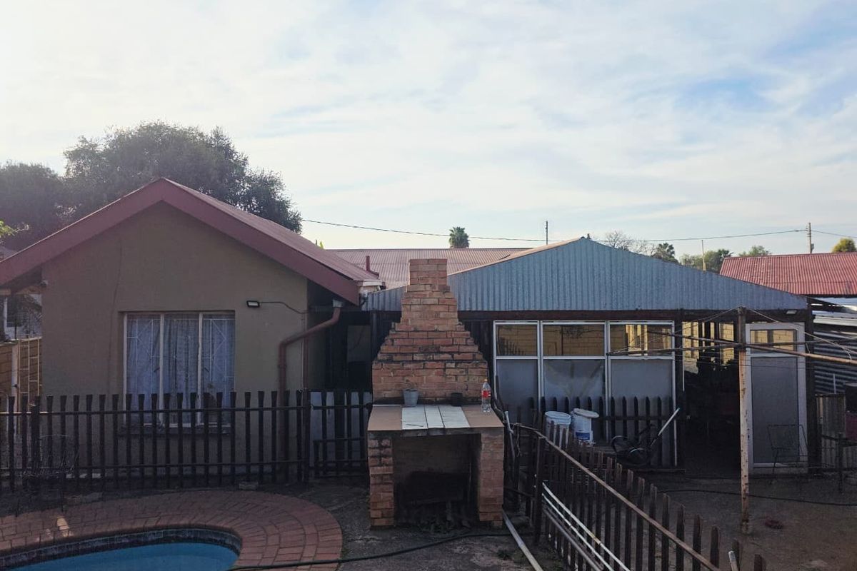 Rear exterior view featuring a swimming pool with paved surround, a brick braai area, and a covered patio structure with metal roofing.