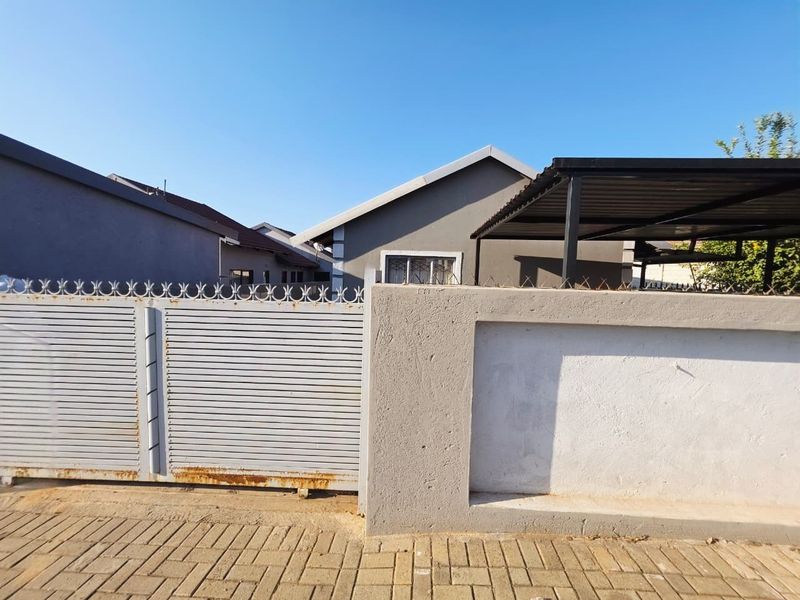 Front view of the property featuring a metal sliding gate, perimeter wall, and a covered carport area.