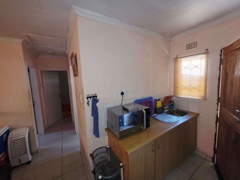 A compact scullery area featuring a stainless steel sink, built-in cabinetry, and tiled flooring, providing a functional secondary prep and wash-up space.