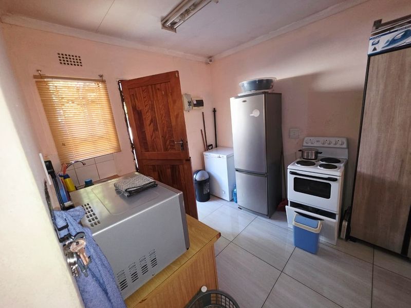 A functional kitchen space featuring tiled flooring, a built-in sink, and timber door access, offering potential for modernization and aesthetic updates.