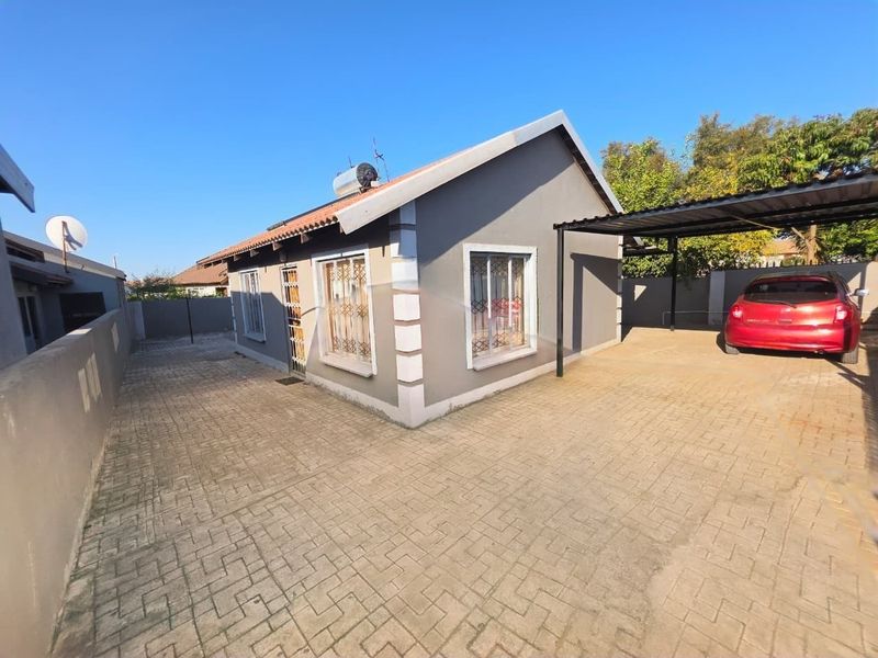 A well-maintained single-story house featuring a paved driveway, carport, and solar geyser, enclosed by a secure boundary wall.