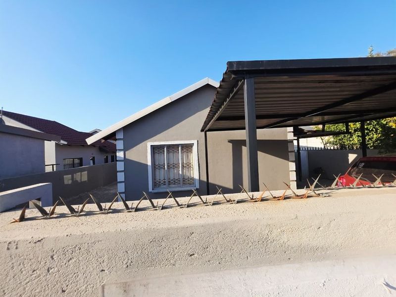 Front view of the property featuring a covered carport, secure boundary wall with metal spikes, and a well-maintained exterior facade.