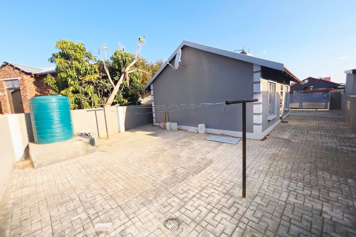 Rear exterior view of the property featuring a paved courtyard, water storage tank, and boundary walling.