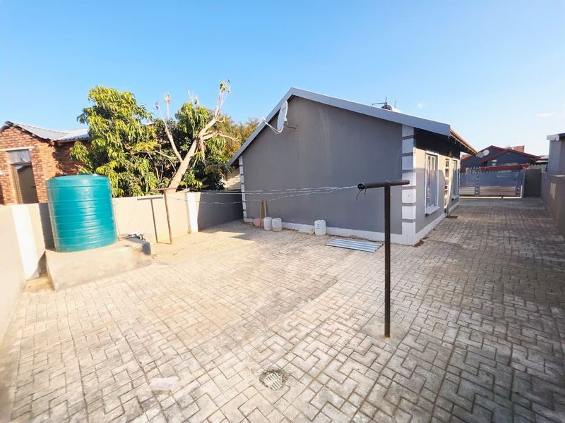 Rear exterior view of the property featuring a paved courtyard, water storage tank, and boundary walling.
