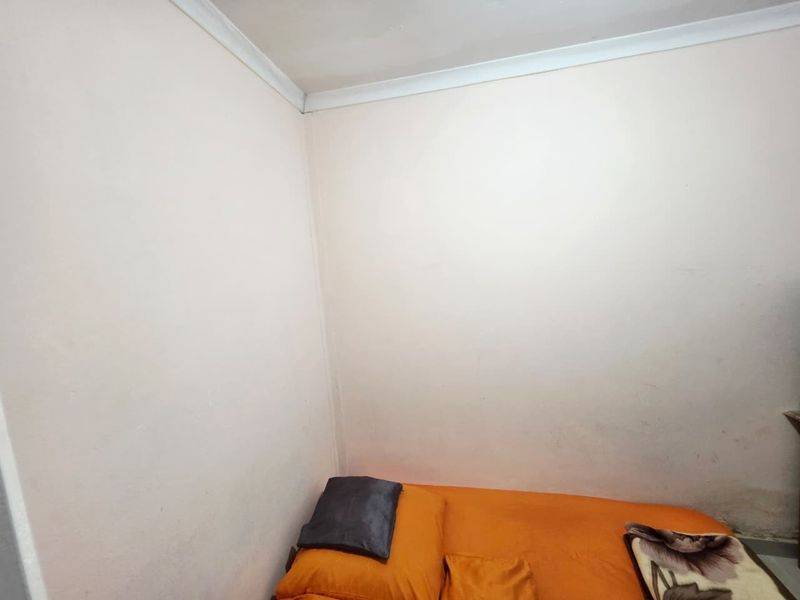 A compact bedroom featuring plain walls with coving, showing signs of wear and requiring cosmetic updates.