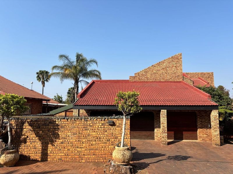 Front view of a face brick house featuring a double garage, tiled roof, and paved driveway with a secure boundary wall.