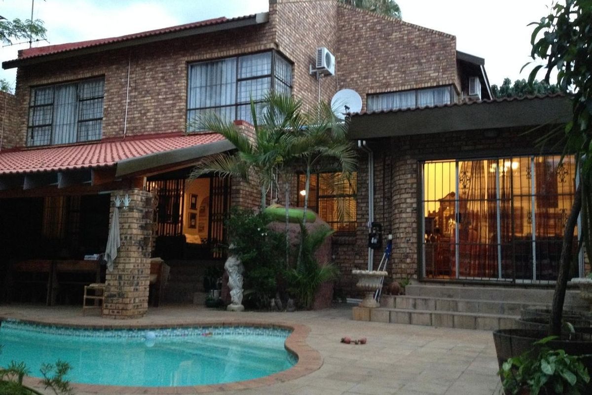 Rear view of a double-story brick house featuring a swimming pool, paved patio area, and sliding door access to the interior living spaces.