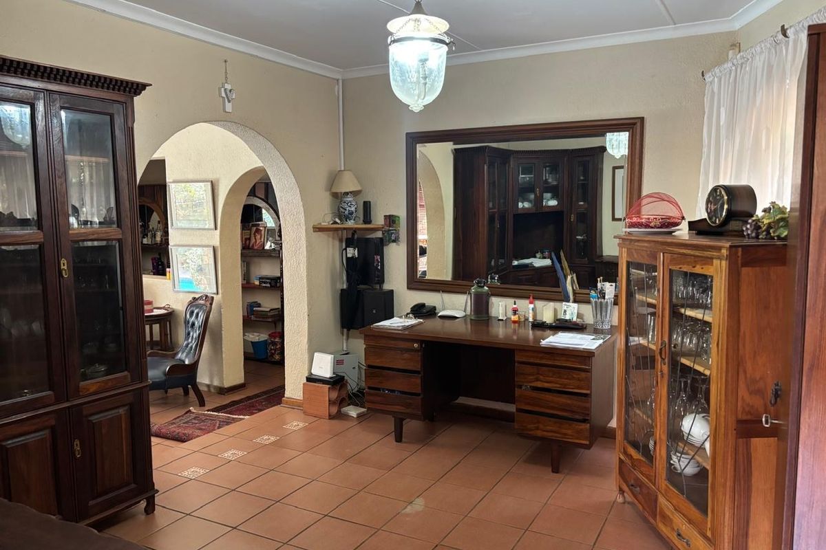 A living area featuring terracotta floor tiles, an arched architectural opening, and a large wall-mounted mirror, offering a traditional layout with potential for modernization.