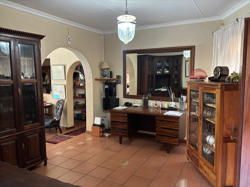 A living area featuring terracotta floor tiles, an arched architectural opening, and a large wall-mounted mirror, offering a traditional layout with potential for modernization.