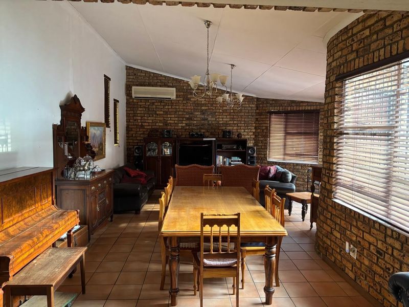 Spacious open-plan living and dining area featuring exposed brick walls, vaulted ceilings, tiled flooring, and large windows with venetian blinds.