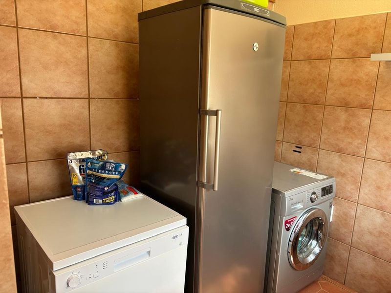 A functional laundry area featuring full-height ceramic wall tiling and tiled flooring, providing a practical space for utility appliances.