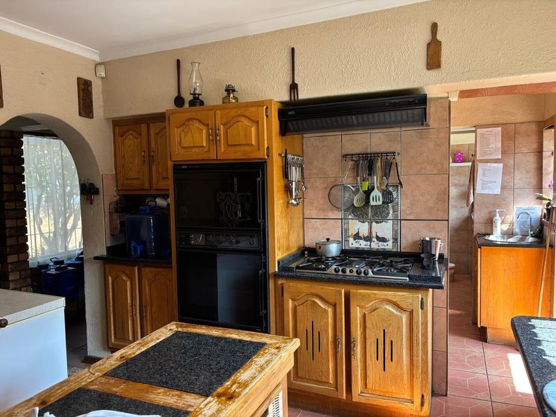 A functional kitchen featuring traditional wooden cabinetry, granite countertops, a gas hob with extractor fan, and tiled flooring with an adjacent scullery area.