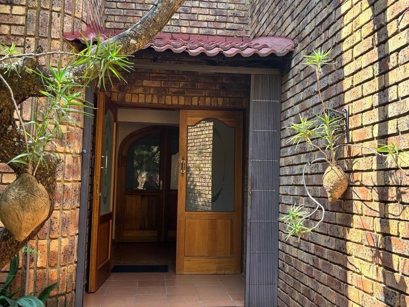 A welcoming entrance featuring face brick walls, tiled flooring, and classic wooden double doors under a small tiled awning.
