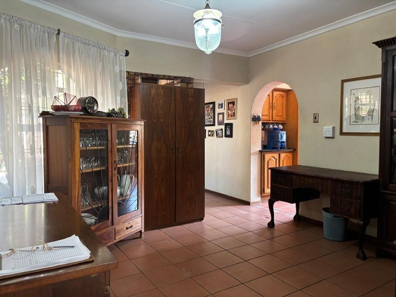 A living area featuring terracotta floor tiles, a coved ceiling, and an arched entryway leading to a kitchen with built-in cabinetry.