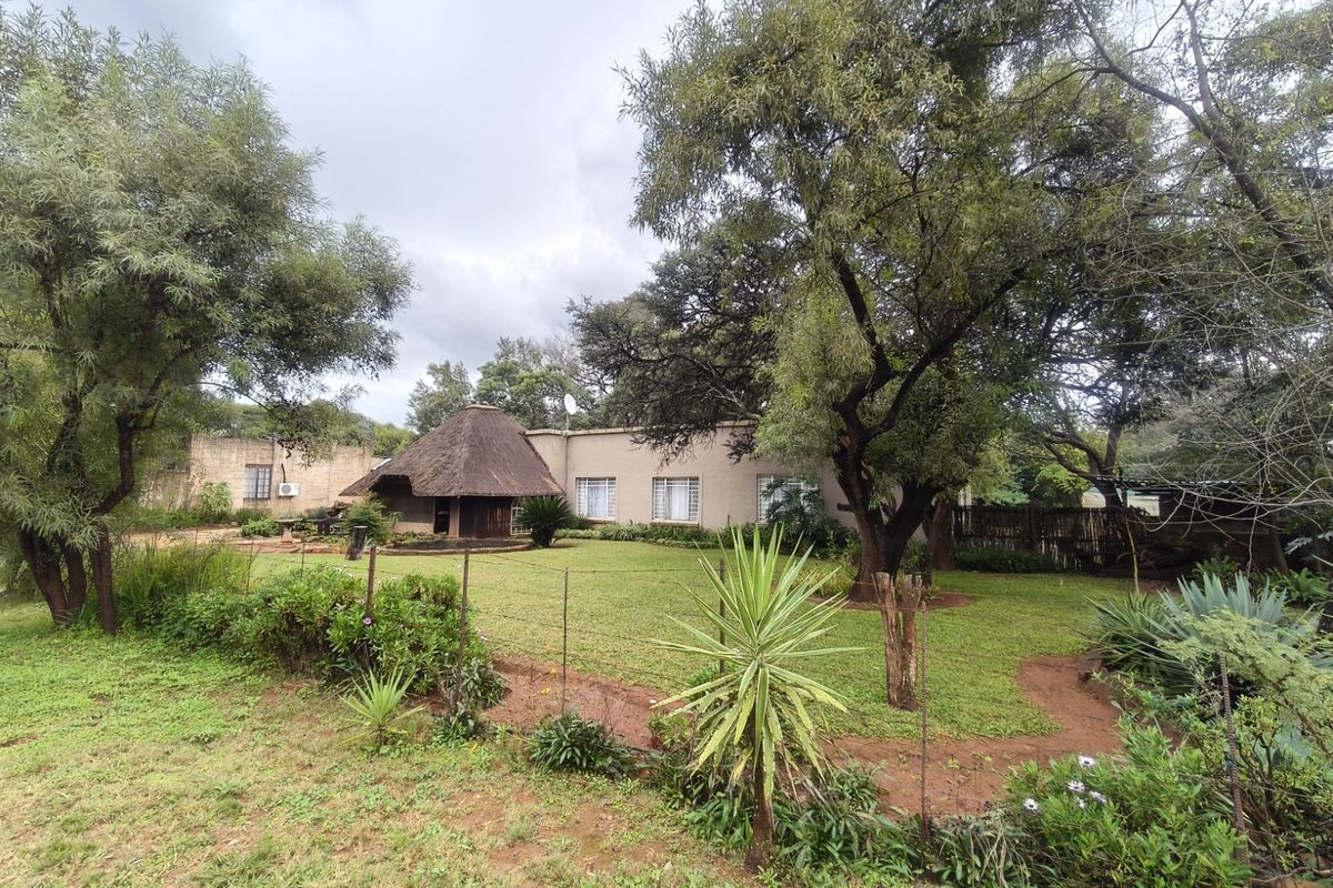 A view of the rear garden and property exterior featuring a traditional thatch roof section and established trees on a spacious farm plot.