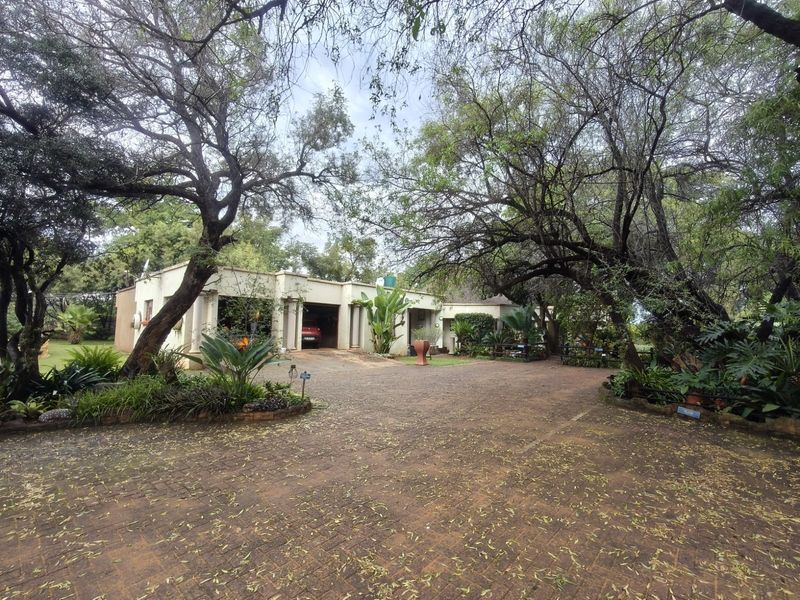 A spacious front exterior view of the farm property featuring a large paved driveway, established mature trees, and a garage entrance.