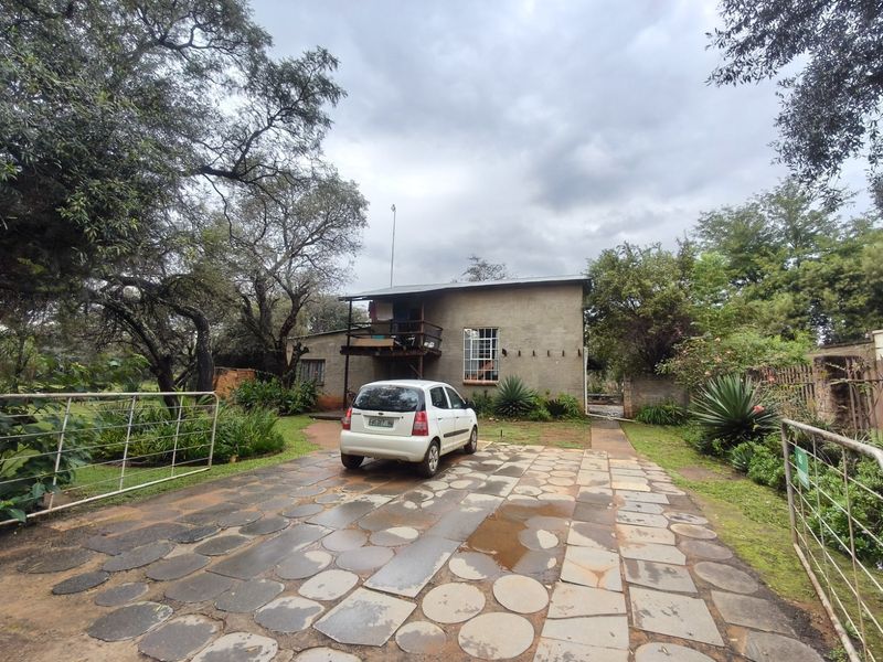 Front view of a farm property featuring a stone paved driveway, metal gate, and a two-story structure with a wooden balcony.