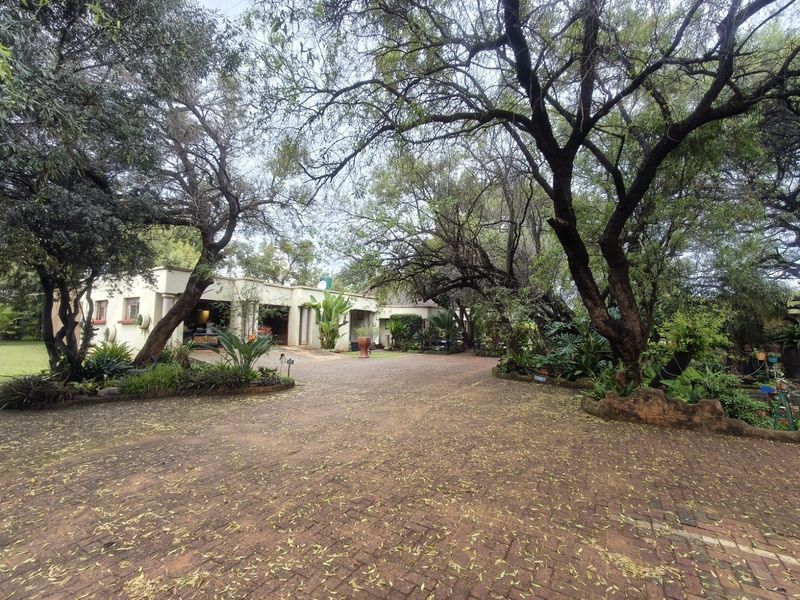A spacious paved driveway leading to the front entrance of the farm property, surrounded by mature trees and established garden landscaping.