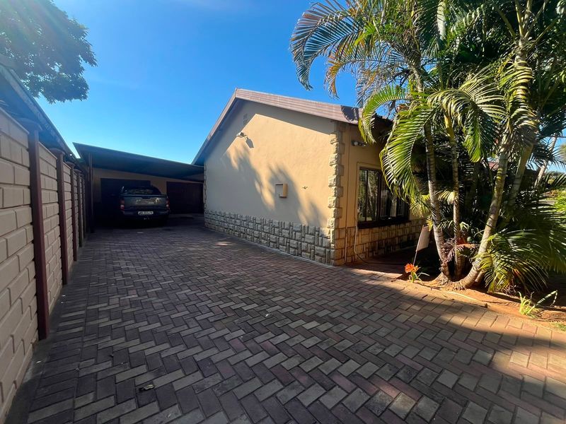 A well-maintained front exterior view featuring a paved driveway, a covered carport, and attractive stone cladding accents on the building facade.