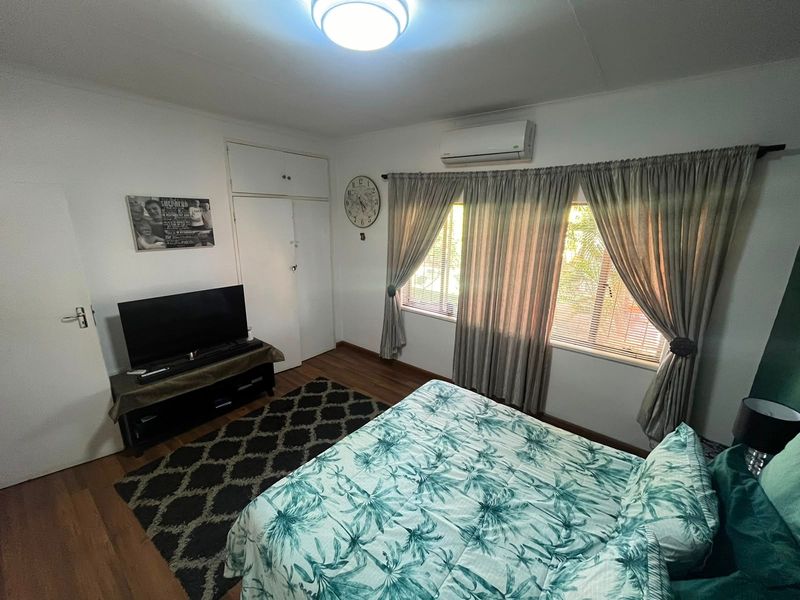 A functional bedroom featuring laminate flooring, a built-in cupboard, and a wall-mounted air conditioning unit.