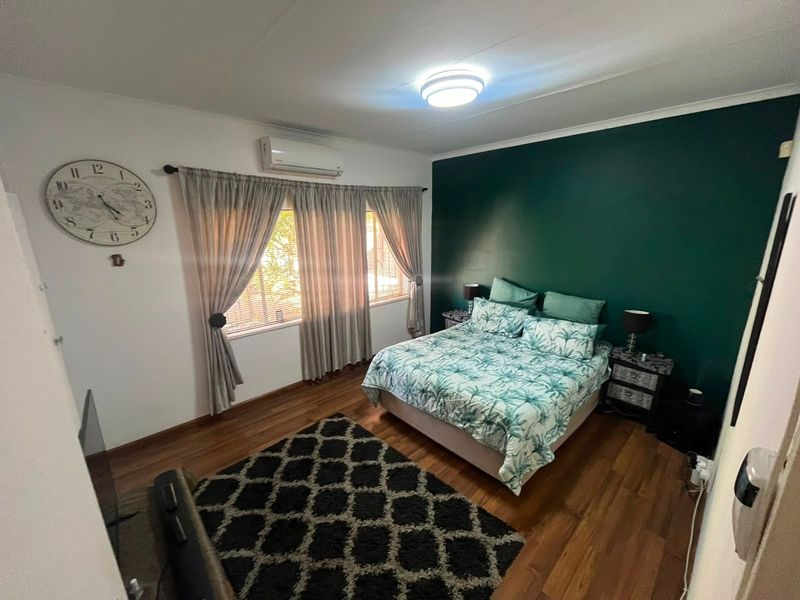 A well-maintained bedroom featuring laminate flooring, an air conditioning unit, and a feature wall.
