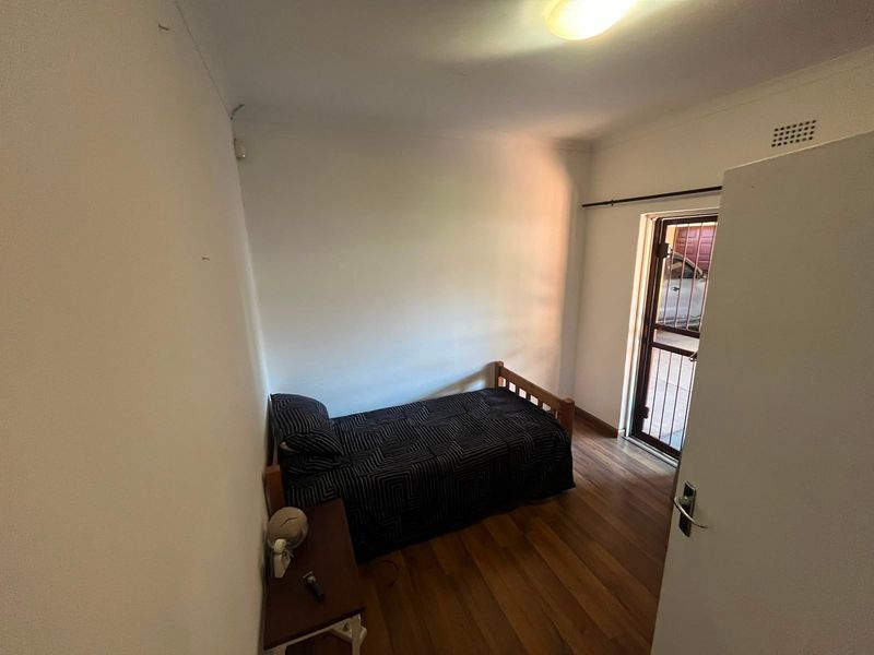 A functional bedroom featuring hardwood flooring, a security gate leading to the exterior, and neutral wall finishes.