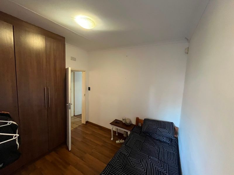 A functional bedroom featuring laminate flooring and a built-in wooden wardrobe, providing essential storage space.