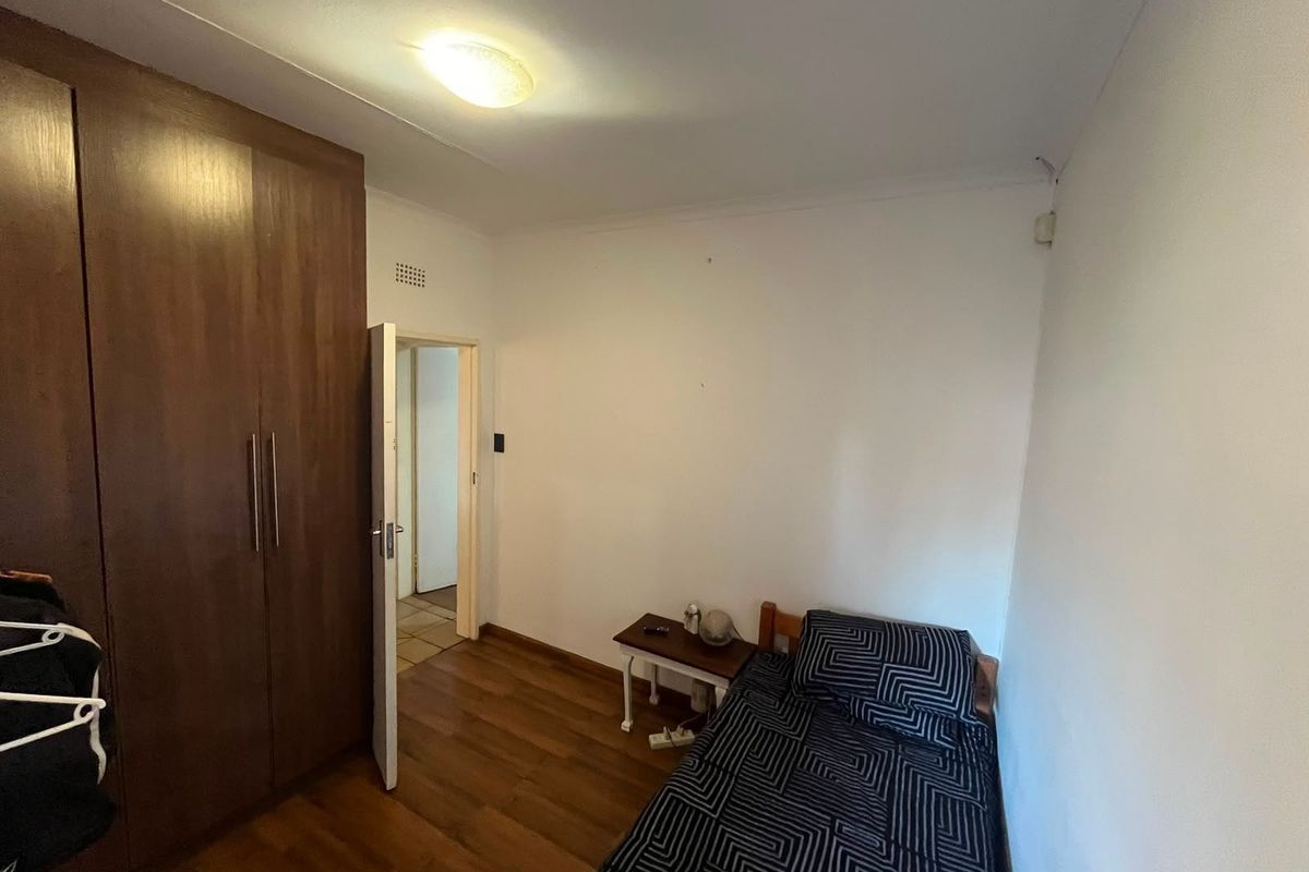 A functional bedroom featuring laminate flooring and a built-in wooden wardrobe, providing essential storage space.
