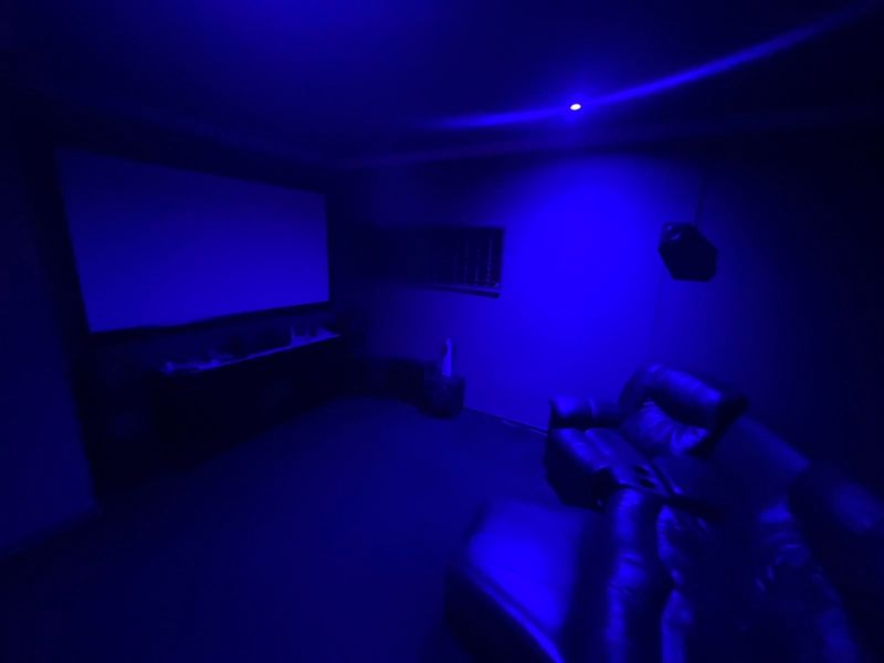 A dedicated cinema room featuring a large projector screen and integrated audio setup, illuminated by blue ambient lighting.