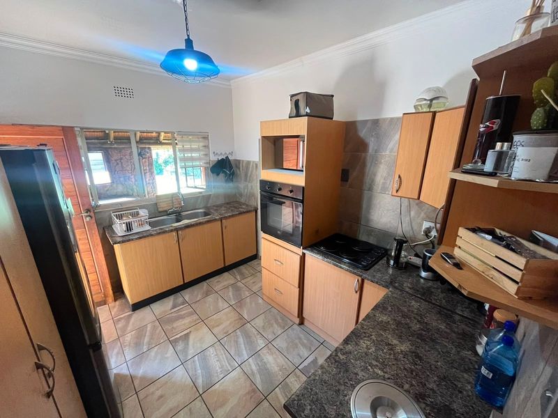 A functional kitchen featuring wood-finish cabinetry, granite-look laminate countertops, built-in oven and hob, tiled backsplash, and tiled flooring.