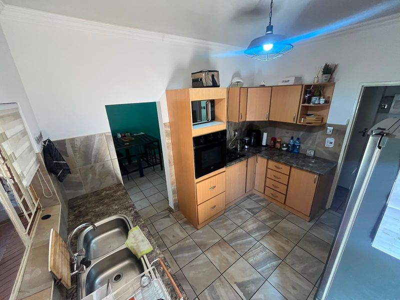 A functional kitchen featuring light wood-finish cabinetry, built-in oven and microwave, double sink, and durable tiled flooring with an adjacent dining area.