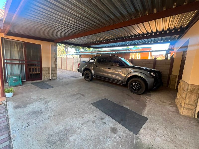 A covered carport or garage area featuring a corrugated metal roof, concrete flooring, and stone-clad pillars.