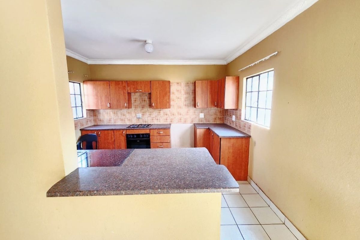 A functional kitchen featuring wooden cabinetry, laminate countertops, a built-in oven with gas hob, and tiled flooring, offering a practical layout for daily use.