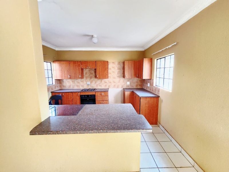 A functional kitchen featuring wooden cabinetry, laminate countertops, a built-in oven with gas hob, and tiled flooring, offering a practical layout for daily use.
