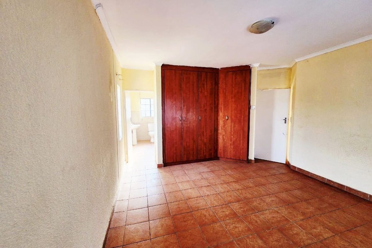 An empty bedroom featuring tiled flooring, built-in wooden cupboards, and direct access to an en-suite bathroom.