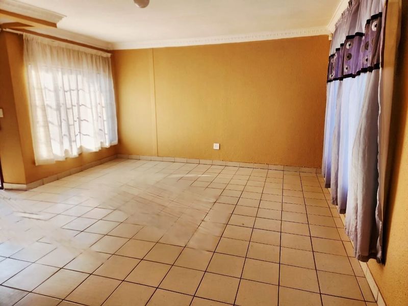 A spacious, empty living room featuring neutral tiled flooring and decorative ceiling cornicing, offering a blank canvas for interior design.