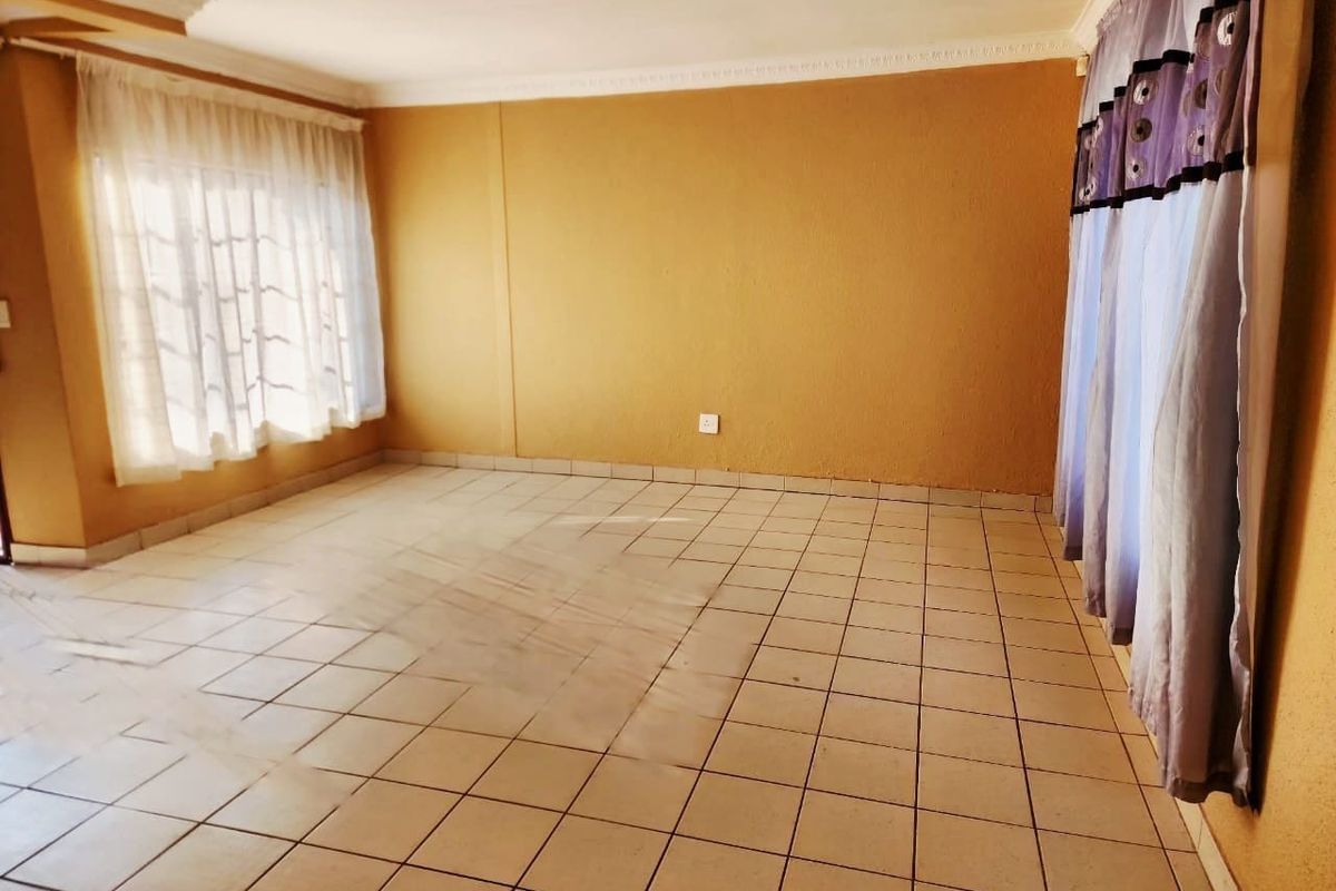 A spacious, empty living room featuring neutral tiled flooring and decorative ceiling cornicing, offering a blank canvas for interior design.