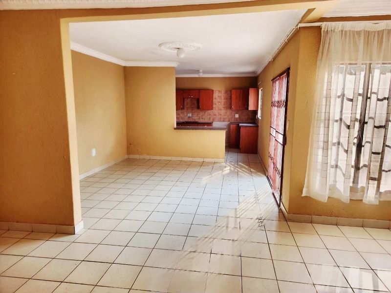 Open plan living area featuring tiled flooring and a connected kitchen with built-in cabinetry and a breakfast counter.