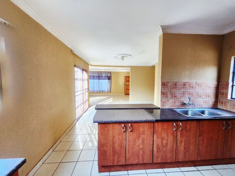 Open plan kitchen and living area featuring granite countertops, wooden cabinetry, and tiled flooring, offering a functional layout with potential for modern updates.