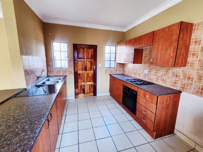A functional kitchen featuring wooden cabinetry, tiled backsplash, built-in oven and hob, and tiled flooring, offering a practical layout for culinary activities.