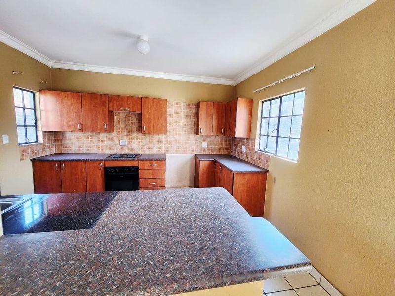 A functional kitchen featuring wooden cabinetry, laminate countertops, a built-in oven, gas hob, and a breakfast bar, offering a practical layout for daily use.