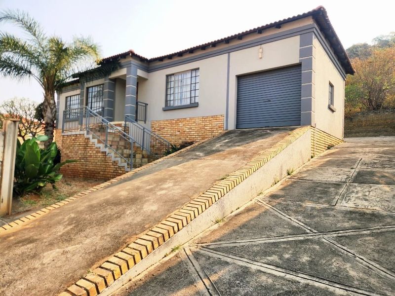 Front elevation of a single-story house featuring a brick and plaster facade, a concrete driveway leading to a garage, and an elevated entrance staircase.