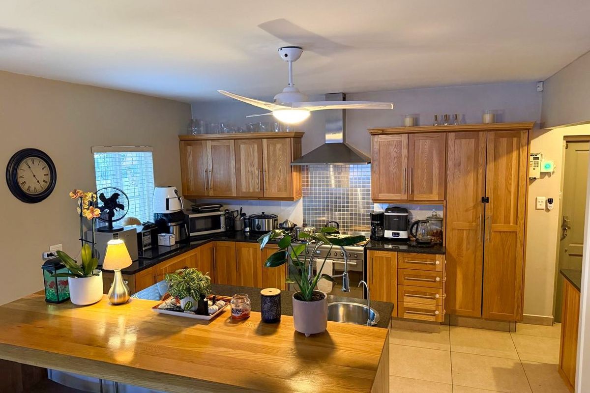 A functional kitchen featuring warm wooden cabinetry, granite countertops, a stainless steel extractor fan, and a breakfast bar island with tiled flooring.