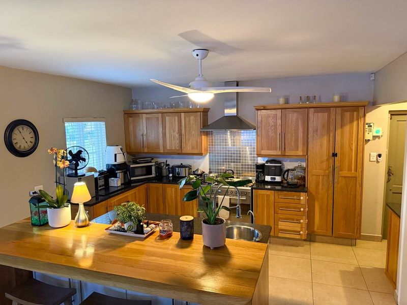 A functional kitchen featuring warm wooden cabinetry, granite countertops, a stainless steel extractor fan, and a breakfast bar island with tiled flooring.