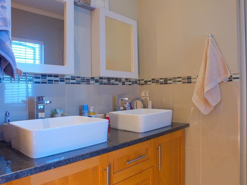 A modern bathroom featuring a double vanity with vessel sinks, granite countertops, wooden cabinetry, and a glass-enclosed shower.