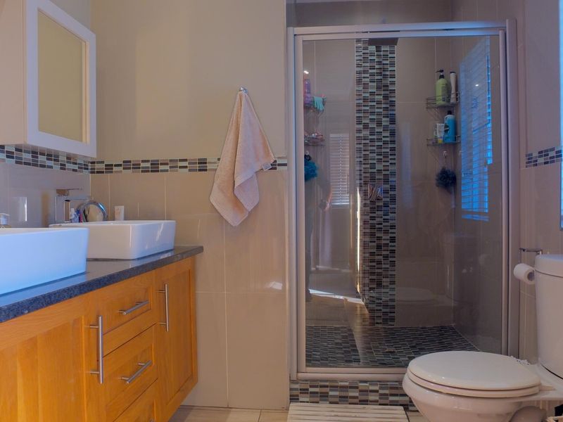 Modern bathroom featuring a double vanity with vessel sinks, a glass-enclosed shower with mosaic tile detailing, and a standard toilet.