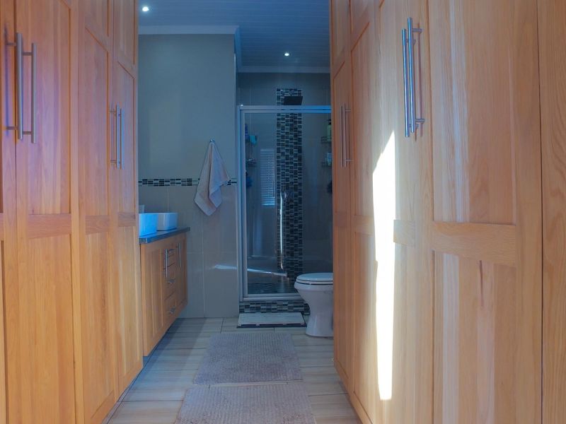 A well-appointed bathroom featuring extensive built-in wooden cabinetry, a double vanity, and a separate glass-enclosed shower area with modern tiling.
