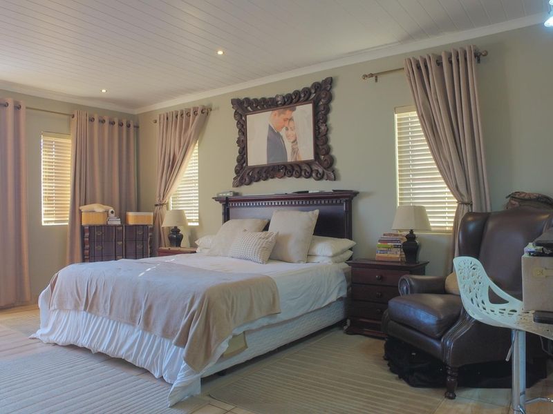 A spacious bedroom featuring tiled flooring, recessed downlighting, and timber-look ceiling paneling, complemented by natural light through venetian blinds.