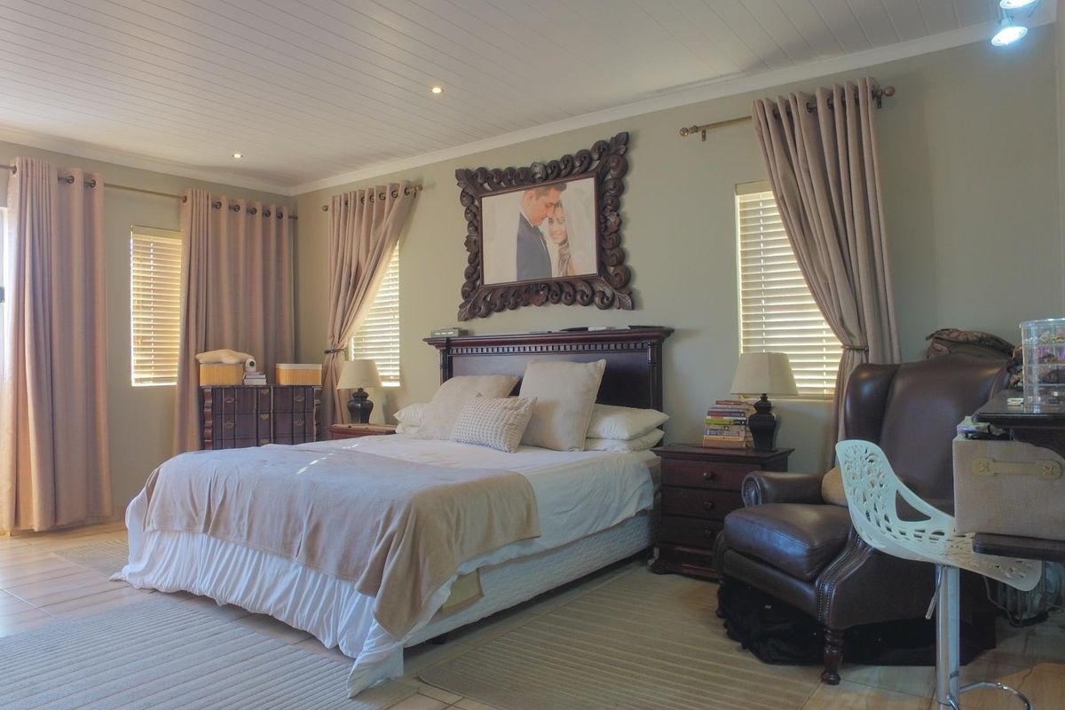 A spacious bedroom featuring tiled flooring, recessed downlighting, and timber-look ceiling paneling, complemented by natural light through venetian blinds.