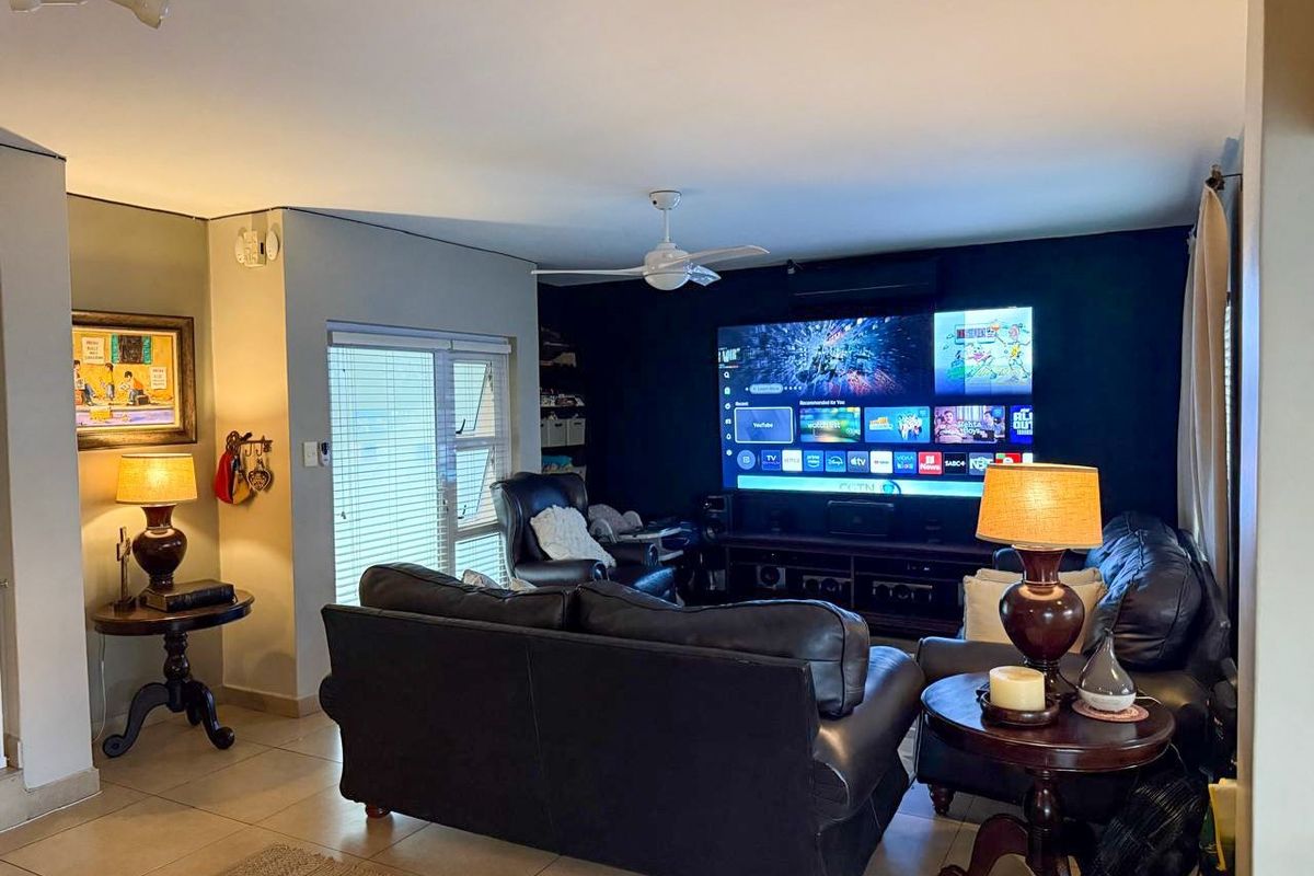 A comfortable living room featuring tiled flooring, a ceiling fan, and an air conditioning unit, with a dedicated media wall setup.